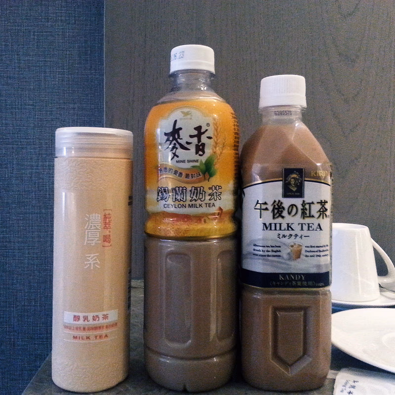 A photo of three bottles of tea and a cup of tea on a table.